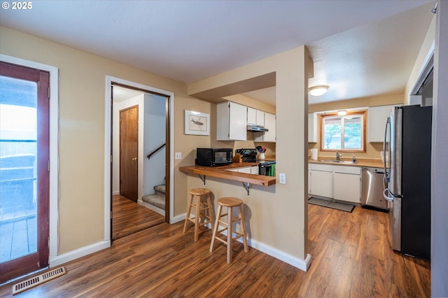 1145 Newport Ave SW, Bandon, OR 97411 - kitchen featuring black appliances, wood finished floors, under cabinet range hood, white cabinetry, and a breakfast bar area