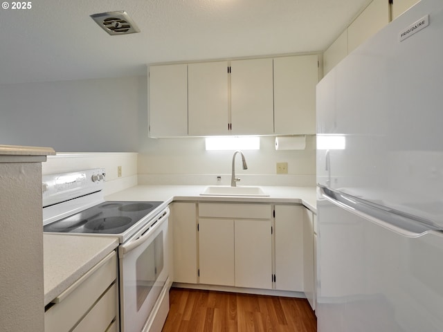 kitchen featuring light wood-style flooring, white appliances, a sink, visible vents, and light countertops