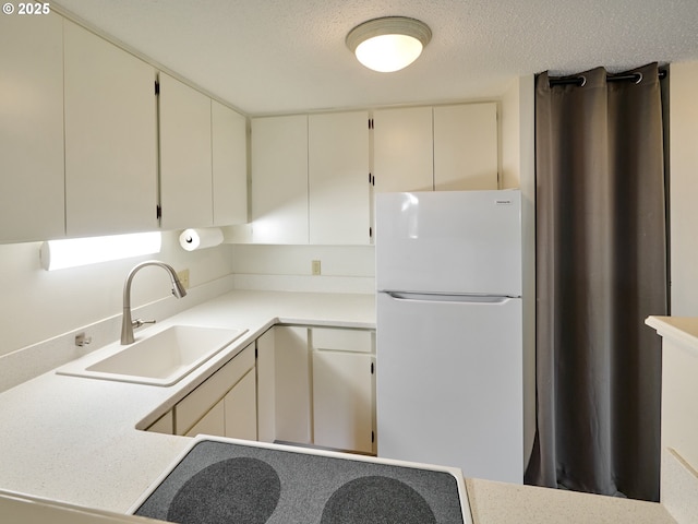 kitchen with freestanding refrigerator, light countertops, a sink, and a textured ceiling