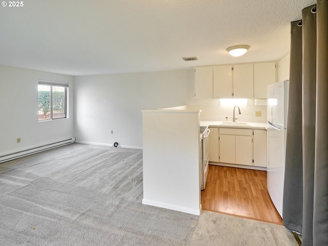 kitchen with light countertops, baseboard heating, a sink, a textured ceiling, and white appliances