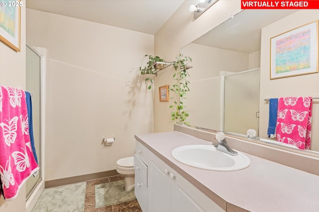 bathroom with vanity, toilet, baseboards, and a shower with shower door