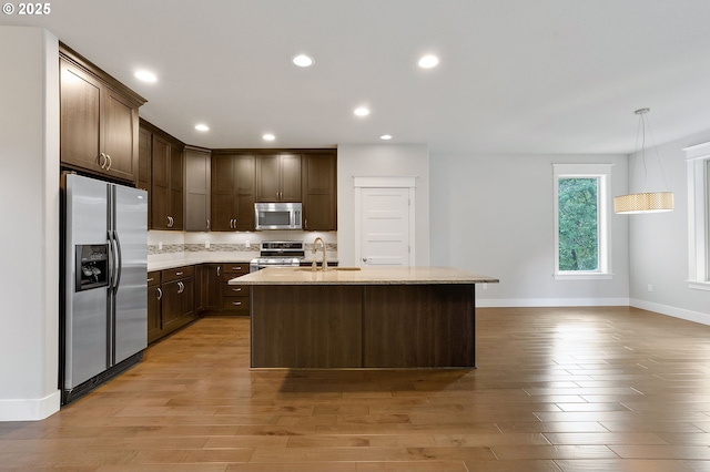 kitchen with decorative light fixtures, light wood-type flooring, a kitchen island with sink, and appliances with stainless steel finishes