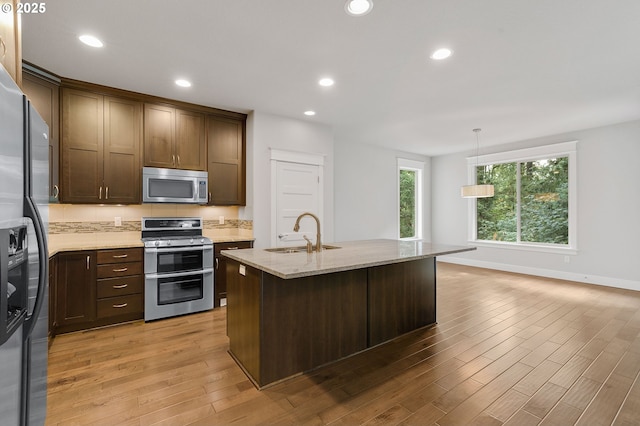 kitchen with light stone countertops, sink, stainless steel appliances, an island with sink, and decorative light fixtures