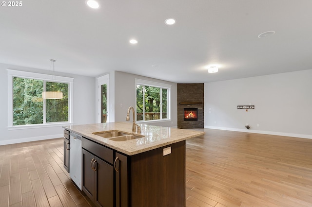 kitchen with sink, light stone counters, light hardwood / wood-style flooring, stainless steel dishwasher, and a center island with sink