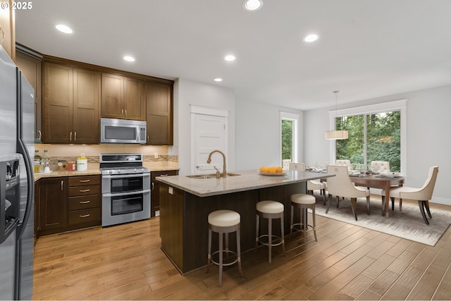 kitchen featuring sink, hanging light fixtures, an island with sink, light hardwood / wood-style floors, and stainless steel appliances