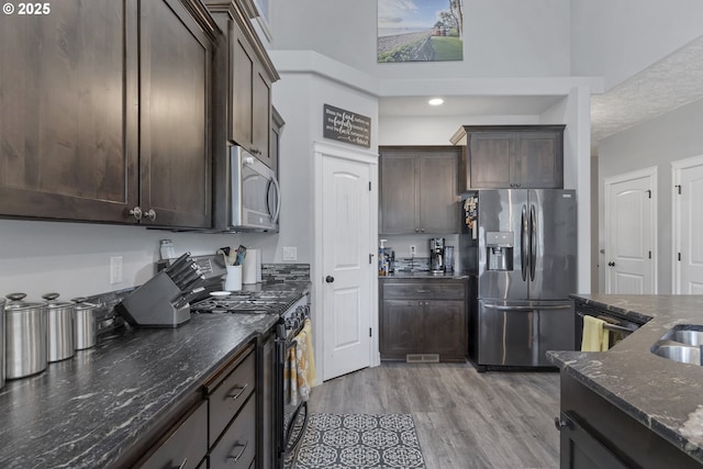 kitchen with dark stone countertops, dark brown cabinetry, appliances with stainless steel finishes, and light wood-style flooring