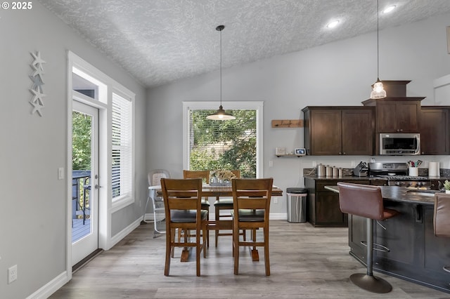 dining space featuring baseboards, a textured ceiling, light wood-type flooring, and lofted ceiling