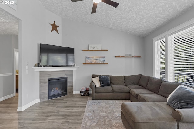 living area with ceiling fan, lofted ceiling, a fireplace, wood finished floors, and a textured ceiling