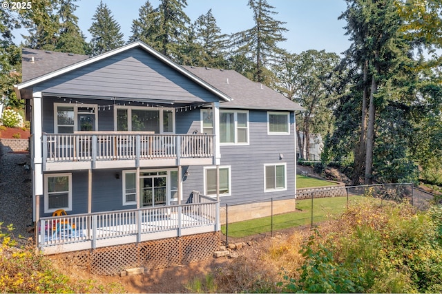 back of property featuring a lawn, a shingled roof, a balcony, and fence