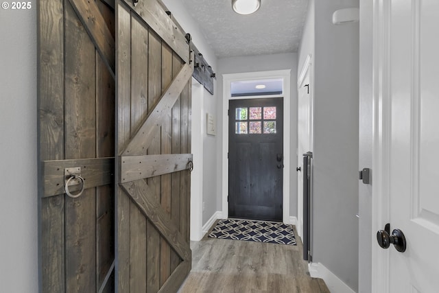 entryway with baseboards, a textured ceiling, a barn door, and wood finished floors