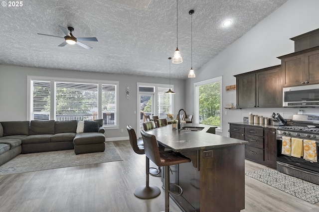 kitchen featuring a breakfast bar area, a sink, stainless steel appliances, dark brown cabinetry, and open floor plan