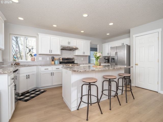 kitchen featuring appliances with stainless steel finishes, a healthy amount of sunlight, a kitchen island, and under cabinet range hood