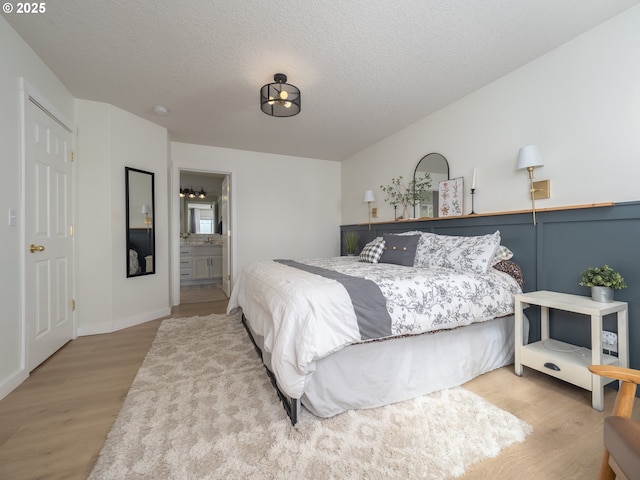 bedroom with a textured ceiling, ensuite bath, wainscoting, and wood finished floors