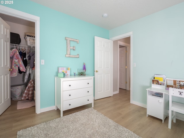 bedroom with light wood-type flooring, baseboards, a walk in closet, and a closet