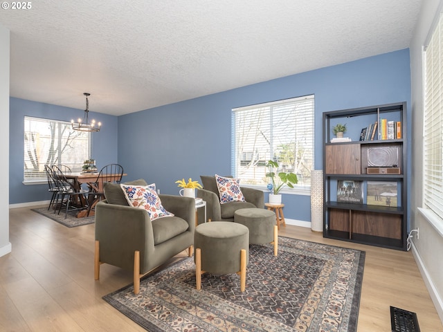 living area with a healthy amount of sunlight, wood finished floors, visible vents, and an inviting chandelier