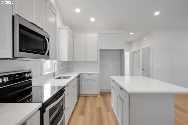 kitchen with sink, light hardwood / wood-style flooring, white cabinetry, stainless steel appliances, and a kitchen island