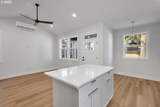 kitchen featuring a kitchen island, an AC wall unit, decorative light fixtures, lofted ceiling, and white cabinets