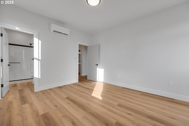 unfurnished bedroom with a walk in closet, a wall mounted AC, and light hardwood / wood-style flooring