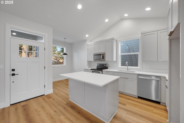 kitchen featuring sink, hanging light fixtures, appliances with stainless steel finishes, a kitchen island, and light hardwood / wood-style floors