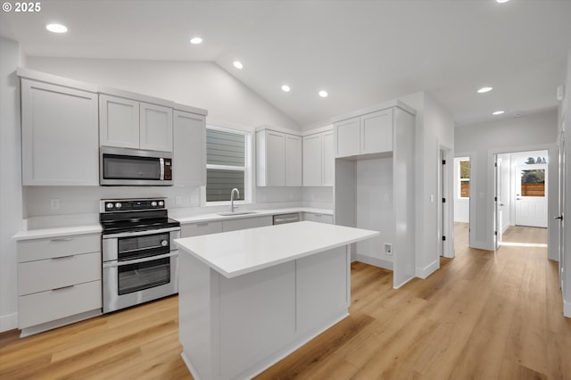 kitchen with lofted ceiling, sink, appliances with stainless steel finishes, a kitchen island, and light hardwood / wood-style floors