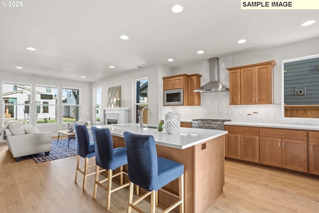 8276 SE Orion Ln, Hillsboro, OR 97123 - kitchen with wall chimney range hood, stainless steel appliances, a kitchen island with sink, a kitchen bar, and light wood-style floors