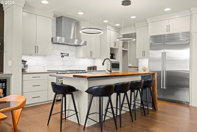 4480 Upper Dr, Lake Oswego, OR 97035 - kitchen featuring built in refrigerator, wall chimney range hood, an island with sink, butcher block counters, and wood finished floors