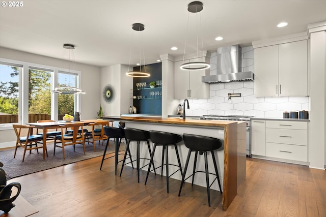 4480 Upper Dr, Lake Oswego, OR 97035 - kitchen featuring wall chimney range hood, an island with sink, tasteful backsplash, wood finished floors, and stove