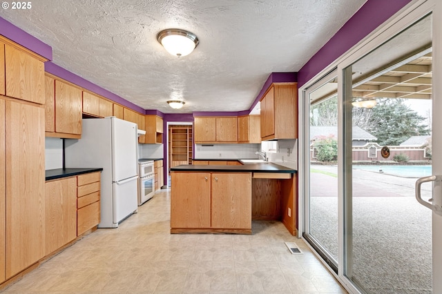 kitchen featuring stove, dark countertops, freestanding refrigerator, a peninsula, and light floors