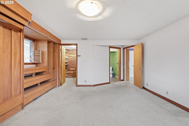 bedroom featuring light carpet, a spacious closet, ensuite bathroom, and baseboards