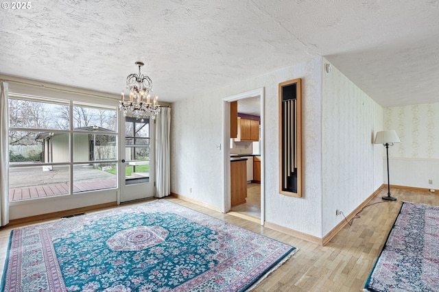 dining area with a notable chandelier, a textured ceiling, hardwood / wood-style floors, wallpapered walls, and baseboards