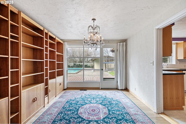 unfurnished dining area featuring baseboards, light wood finished floors, a textured ceiling, a textured wall, and a chandelier