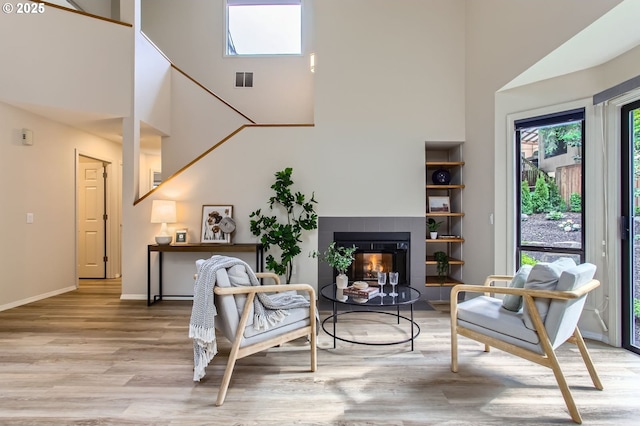 living area with a high ceiling, light wood-style floors, a tile fireplace, and baseboards