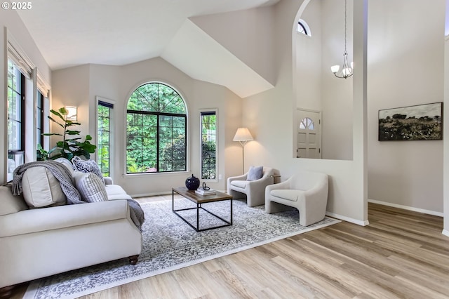 living area featuring wood finished floors, baseboards, lofted ceiling, and a chandelier
