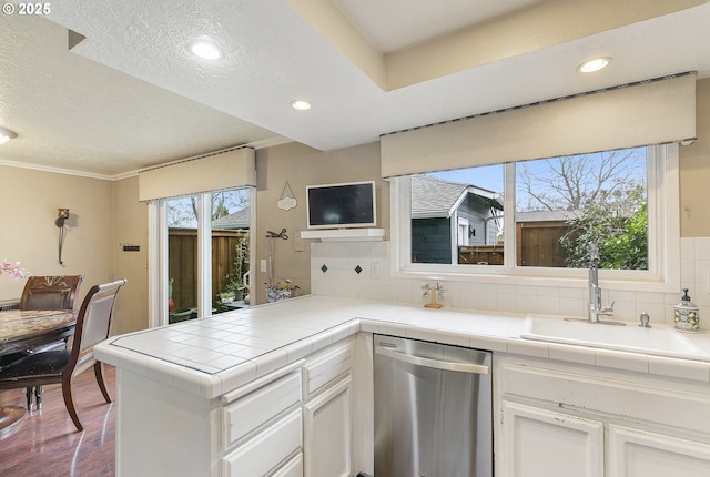 kitchen with tasteful backsplash, white cabinets, tile countertops, stainless steel dishwasher, and a sink