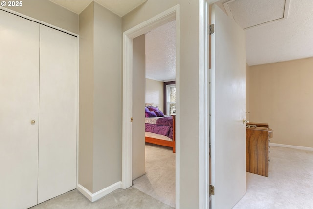 hallway featuring baseboards, a textured ceiling, and light colored carpet