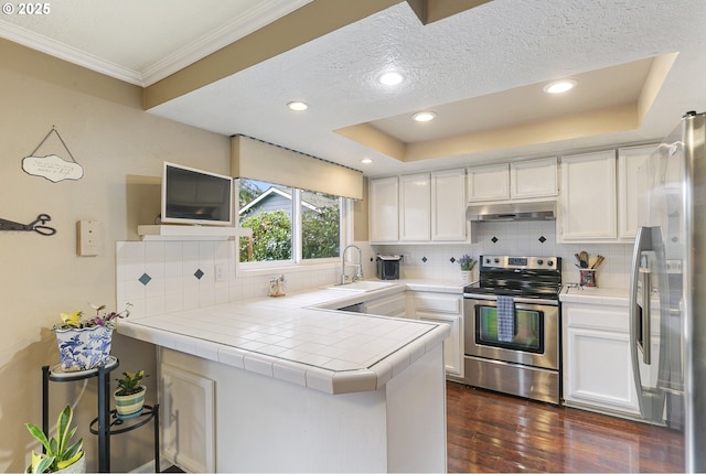 kitchen featuring tile counters, a peninsula, stainless steel appliances, under cabinet range hood, and a sink