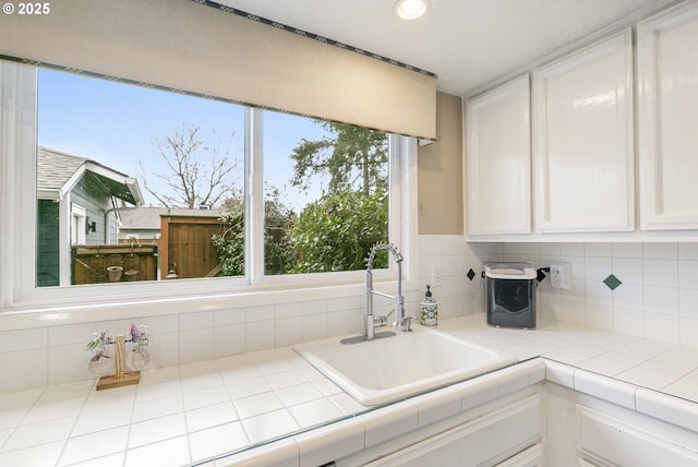 kitchen with tile countertops, a sink, white cabinets, and backsplash