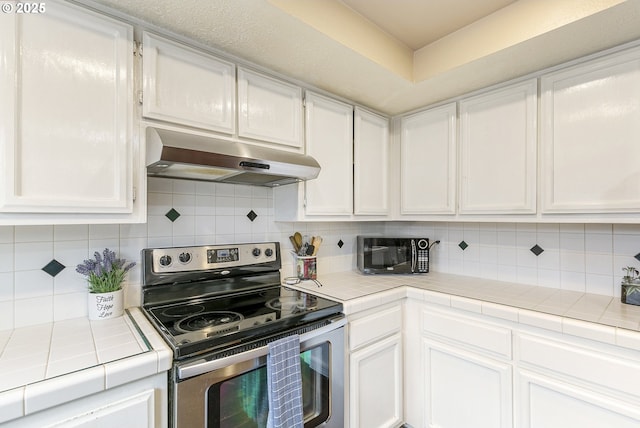 kitchen with tile countertops, white cabinets, black microwave, under cabinet range hood, and stainless steel electric range