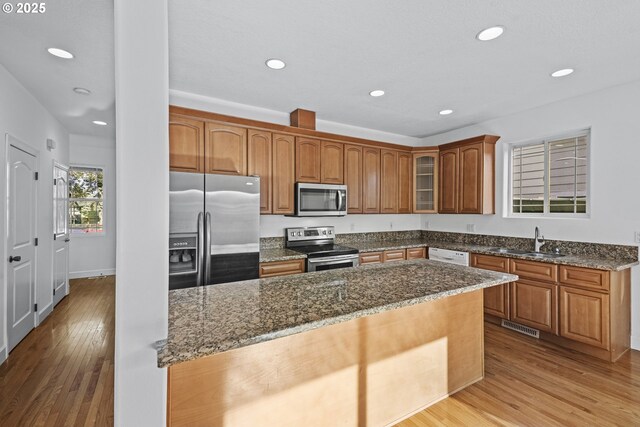 kitchen featuring a center island, sink, dark stone countertops, light hardwood / wood-style flooring, and stainless steel appliances