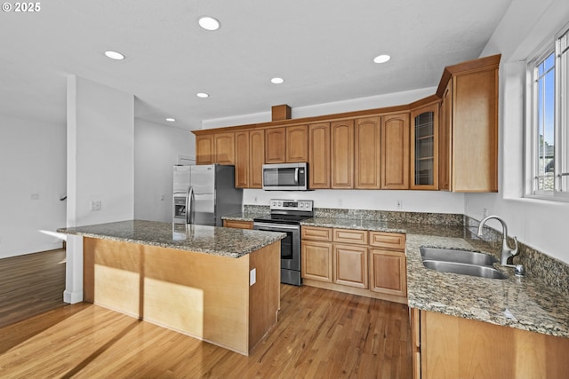 kitchen featuring appliances with stainless steel finishes, a kitchen island, dark stone countertops, sink, and light wood-type flooring