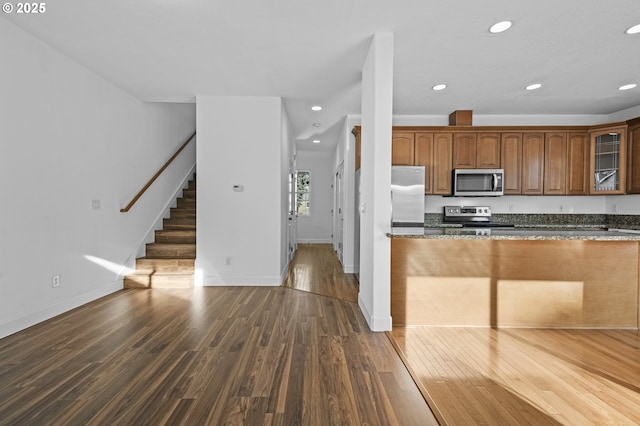 kitchen with dark wood-type flooring, appliances with stainless steel finishes, and dark stone counters