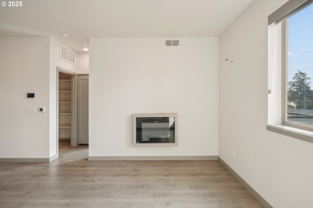 spare room with heating unit, a wealth of natural light, and light hardwood / wood-style flooring