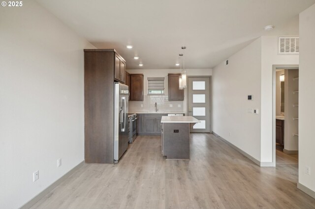 kitchen featuring a kitchen island, decorative light fixtures, stainless steel appliances, sink, and light wood-type flooring