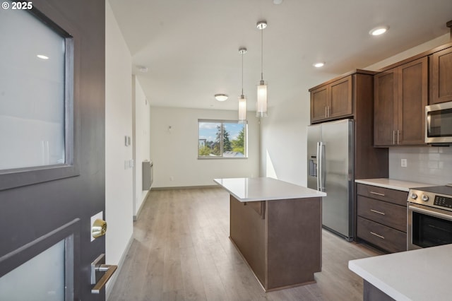 kitchen featuring pendant lighting, appliances with stainless steel finishes, a center island, light hardwood / wood-style floors, and backsplash