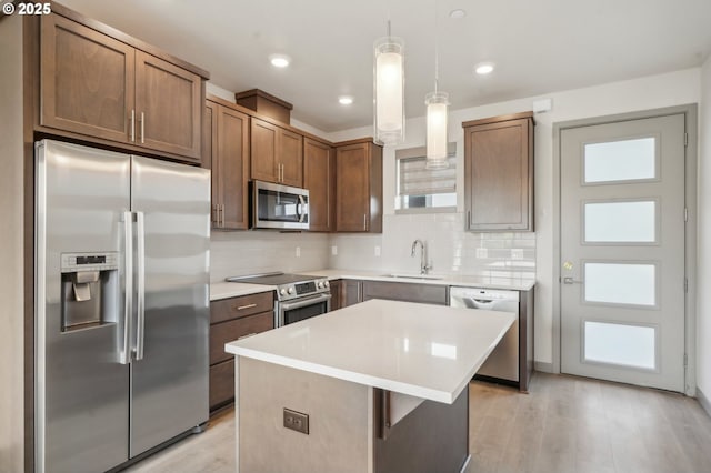 kitchen with appliances with stainless steel finishes, pendant lighting, backsplash, and a kitchen island