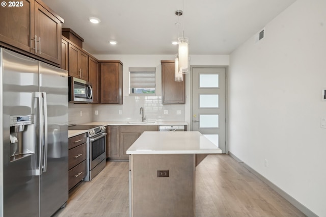 kitchen featuring tasteful backsplash, pendant lighting, a kitchen island, sink, and appliances with stainless steel finishes