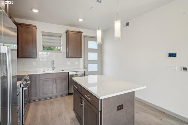 kitchen featuring stainless steel appliances, decorative backsplash, a center island, decorative light fixtures, and sink