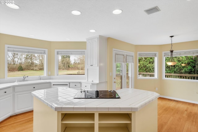 kitchen featuring a center island, light wood-style floors, black electric stovetop, and tile counters