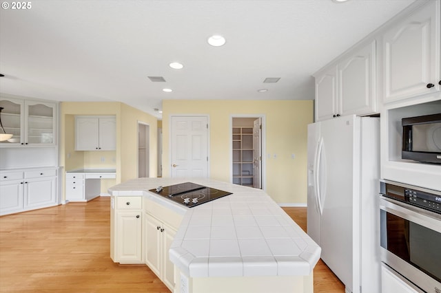 kitchen with light wood finished floors, black appliances, tile counters, white cabinets, and a center island