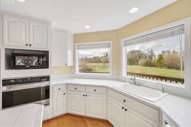 kitchen featuring a sink, white cabinets, black microwave, light countertops, and stainless steel oven